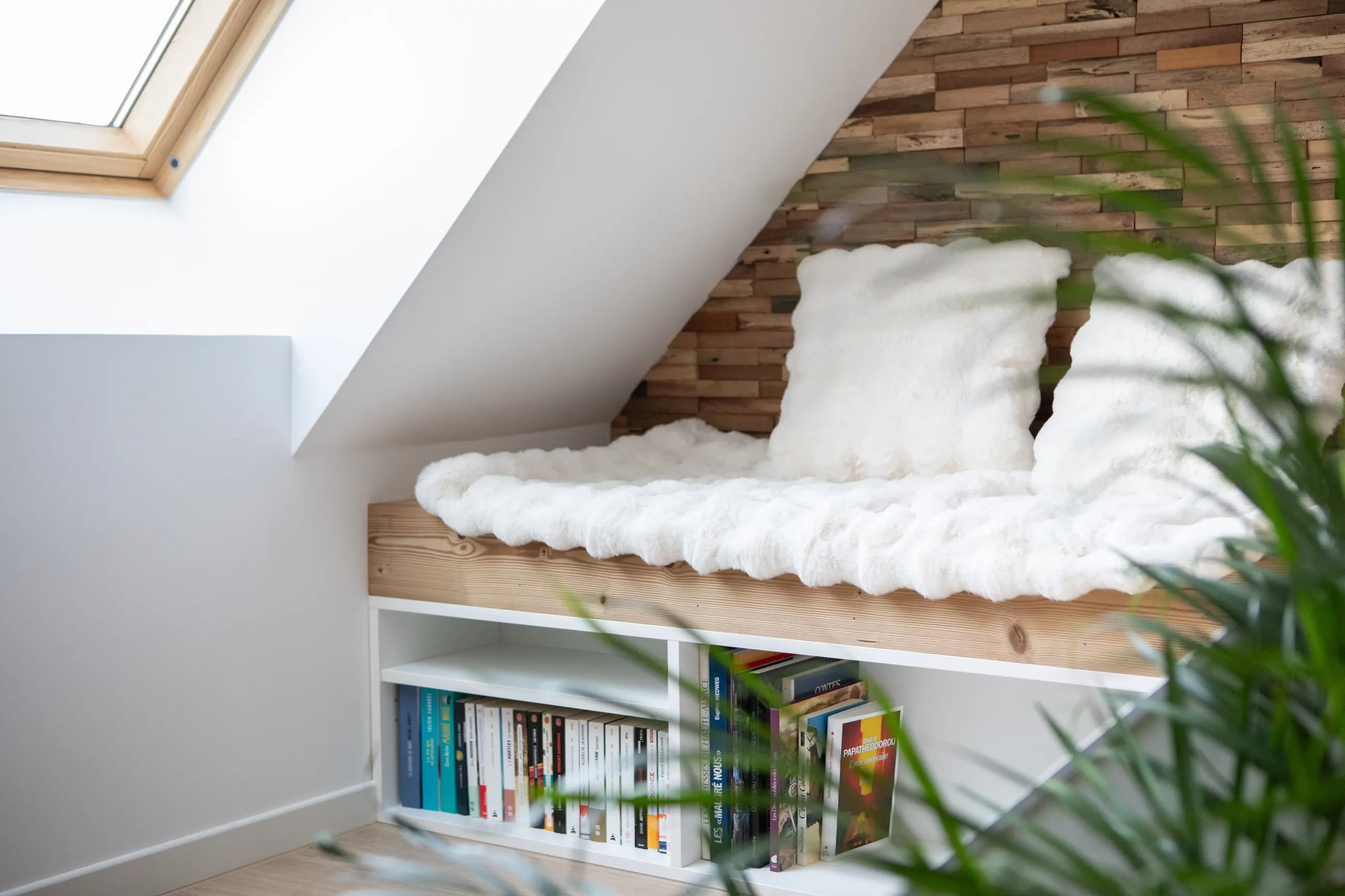 Coin lecture du gîte Porte D avec banquette confortable, coussins duveteux et étagère de livres.