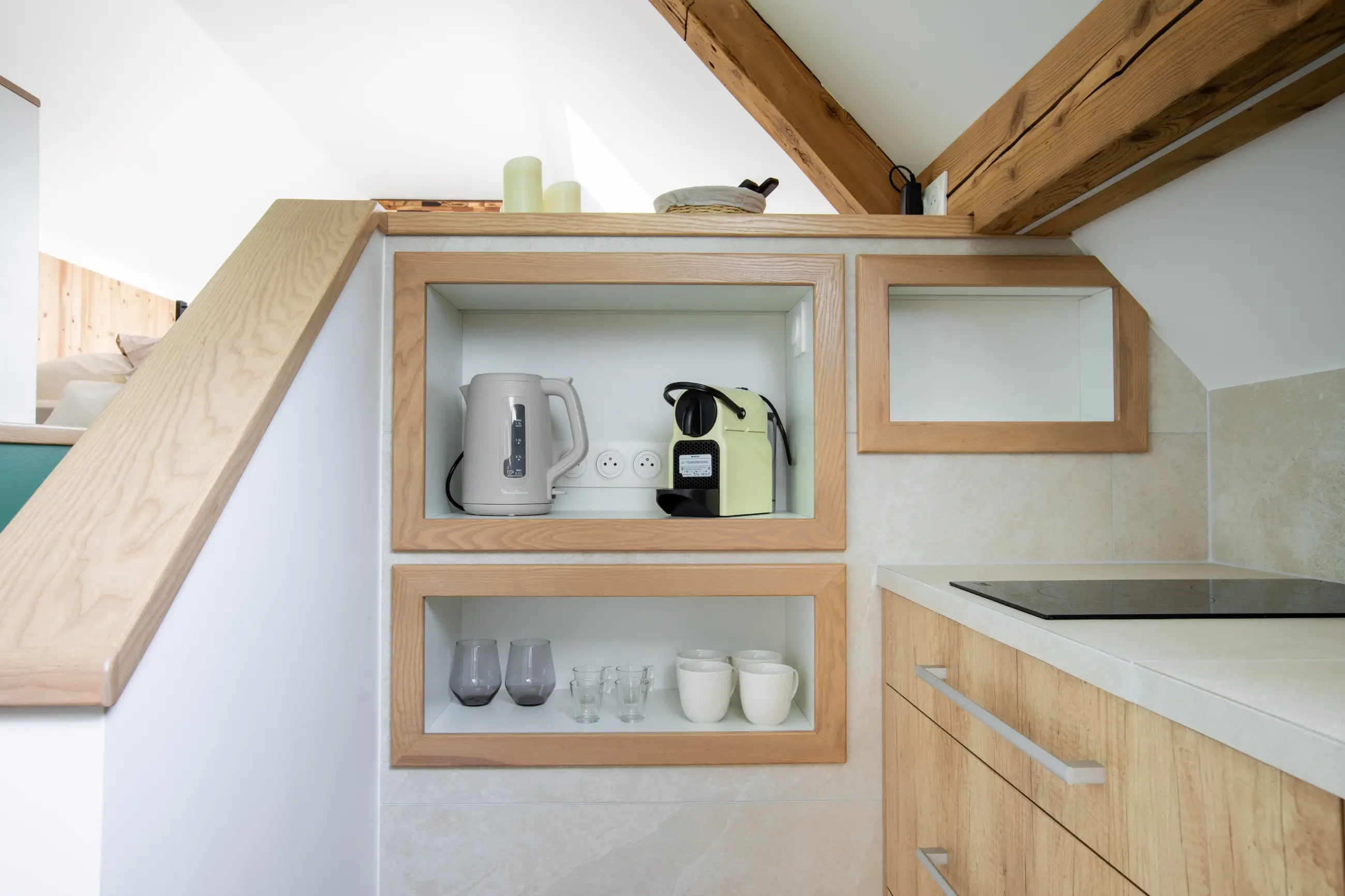 Équipements de la cuisine du gîte Porte D : bouilloire, machine Nespresso, verres et tasses rangés dans des niches en bois.