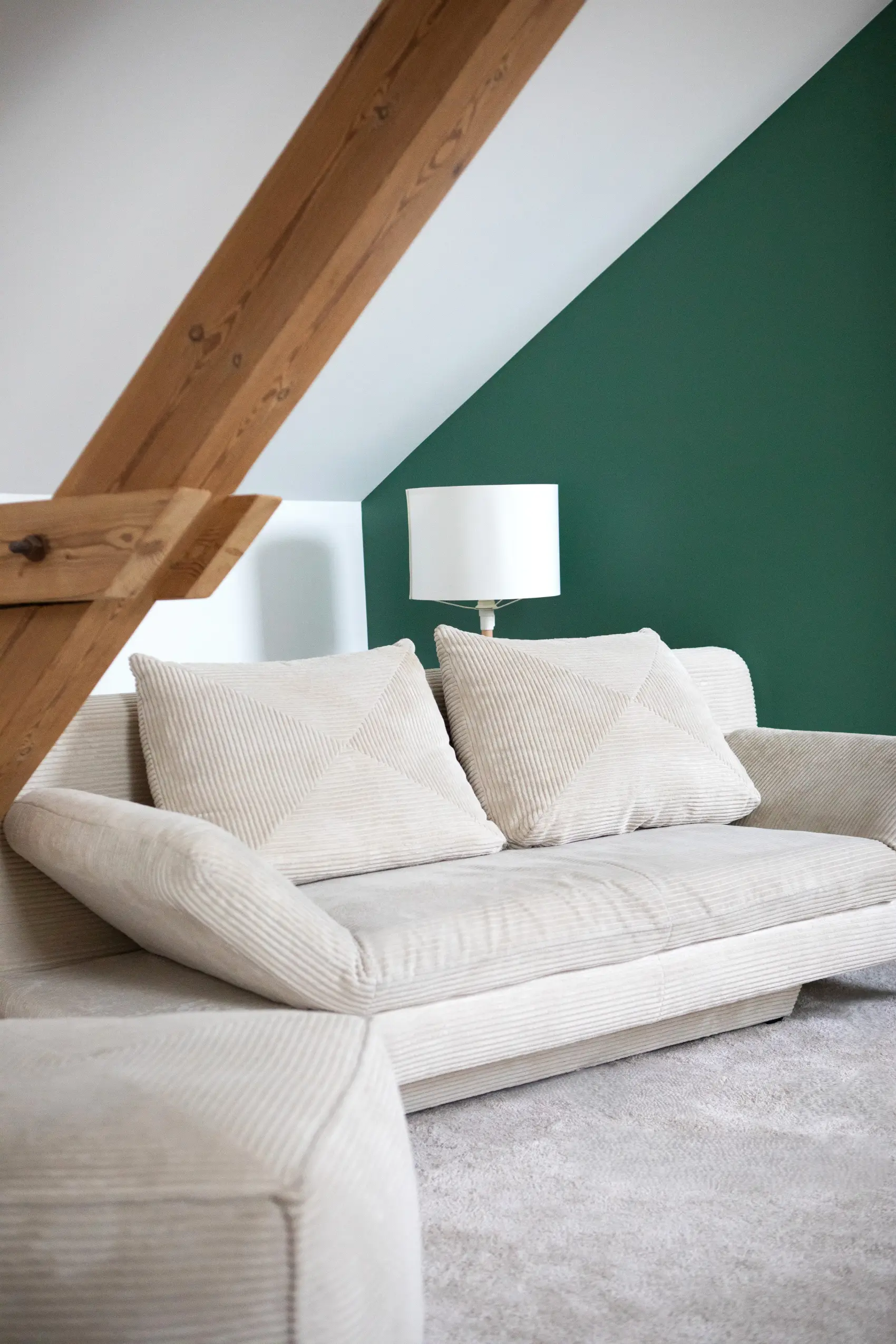 Canapé beige confortable du gîte Porte D, décoré de coussins texturés et poutre en bois.