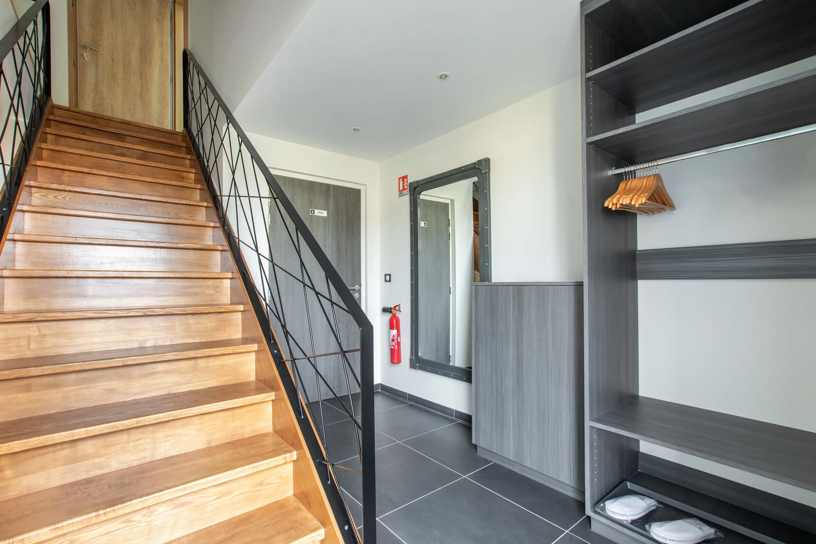 Entrée du gîte Porte D avec escalier en bois, grand miroir et espace de rangement.