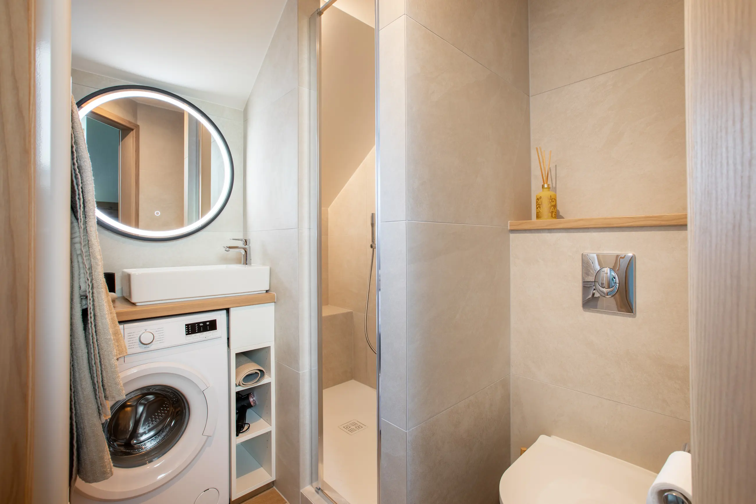 Salle de bain du gîte Porte D avec douche moderne, lavabo, miroir lumineux et toilettes intégrées.